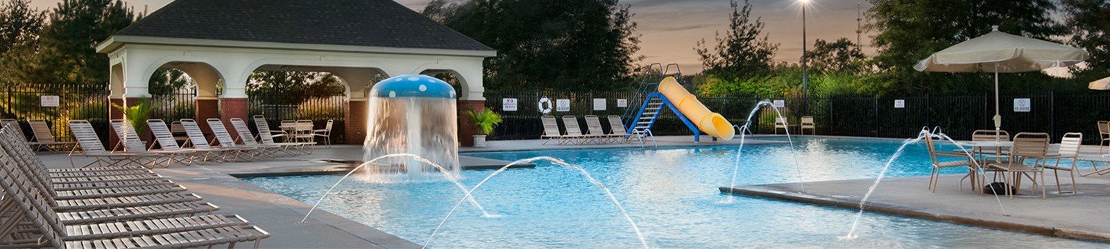 a swimming pool with a water fountain and a pool house in the background